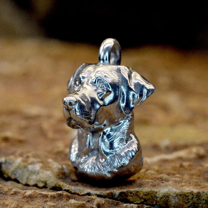 A detailed Labrador Side view sterling silver dog ashes pendant with a textured, metallic finish, standing on a rustic stone surface against a dark, blurred background.