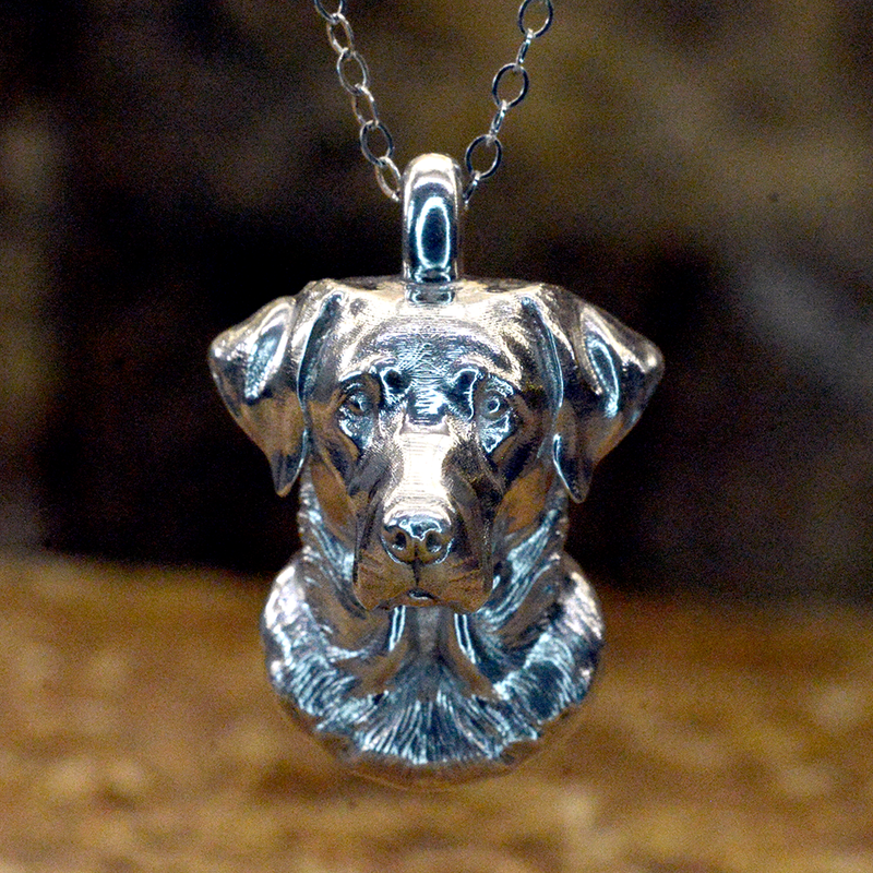 A detailed Labrador Side view sterling silver dog ashes pendant with a textured, metallic finish, standing on a rustic stone surface against a dark, blurred background.