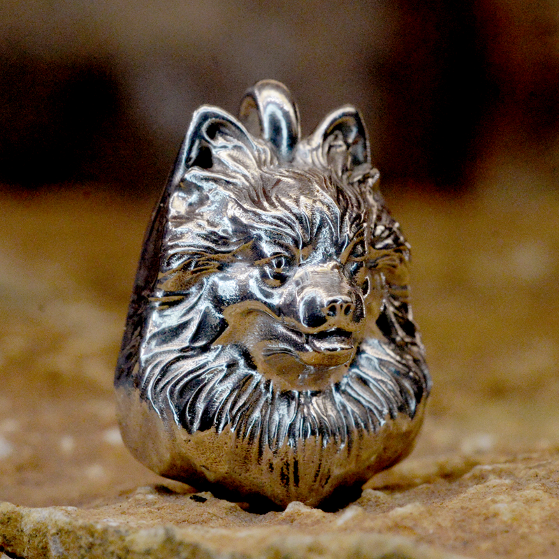 A detailed sterling silver ring shaped like a dog's head, featuring textured engravings and polished highlights, resting on a rustic stone surface.
