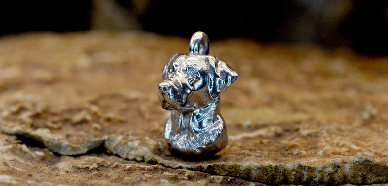 A detailed Labrador Side view sterling silver dog ashes pendant with a textured, metallic finish, standing on a rustic stone surface against a dark, blurred background.